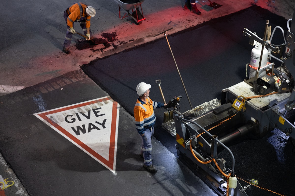 A Streets Division worker in a hard hat and safety vest operating an asphalt paving machine at night