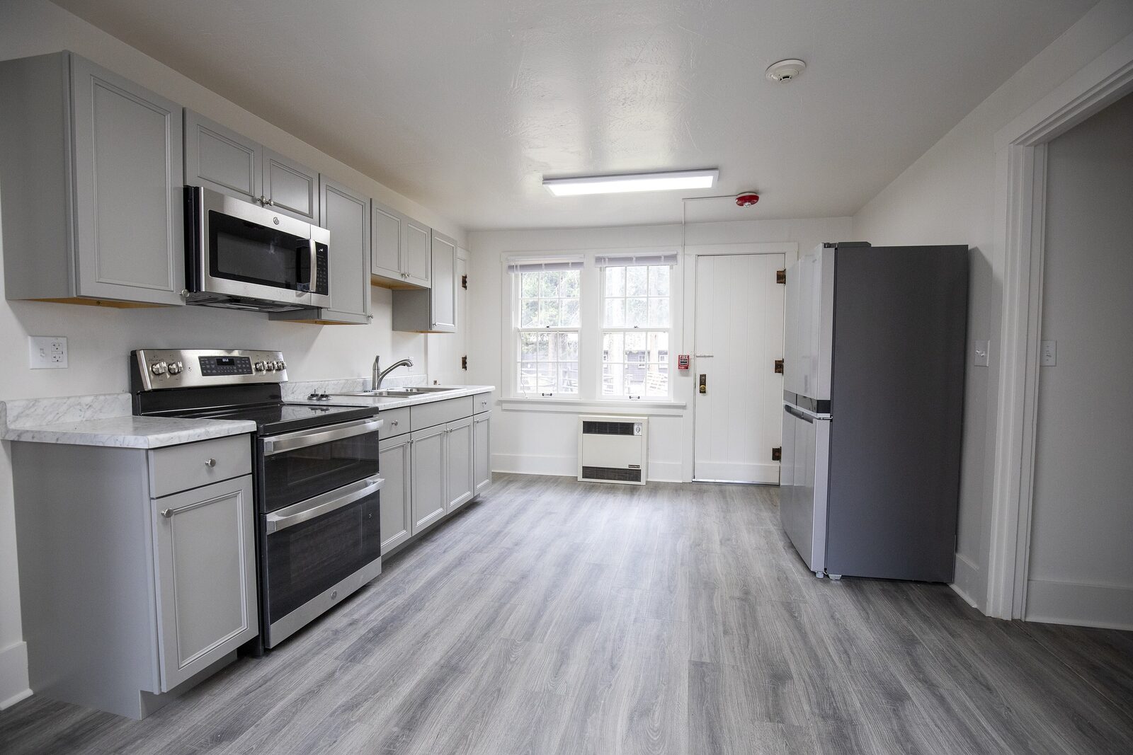 The remodeled kitchen with gray cabinets and plank flooring
