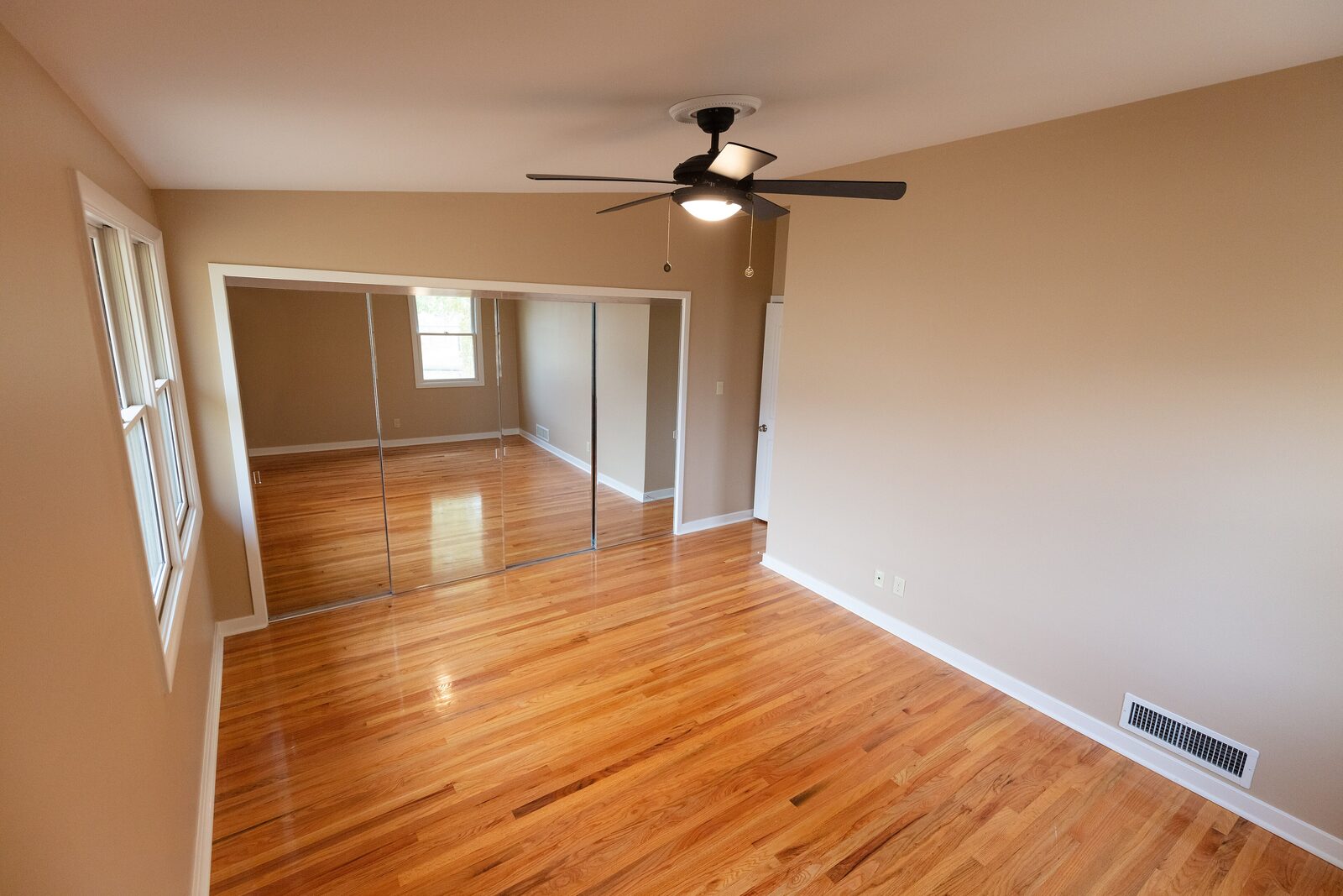 Primary bedroom with mirrored closet doors and refinished floors