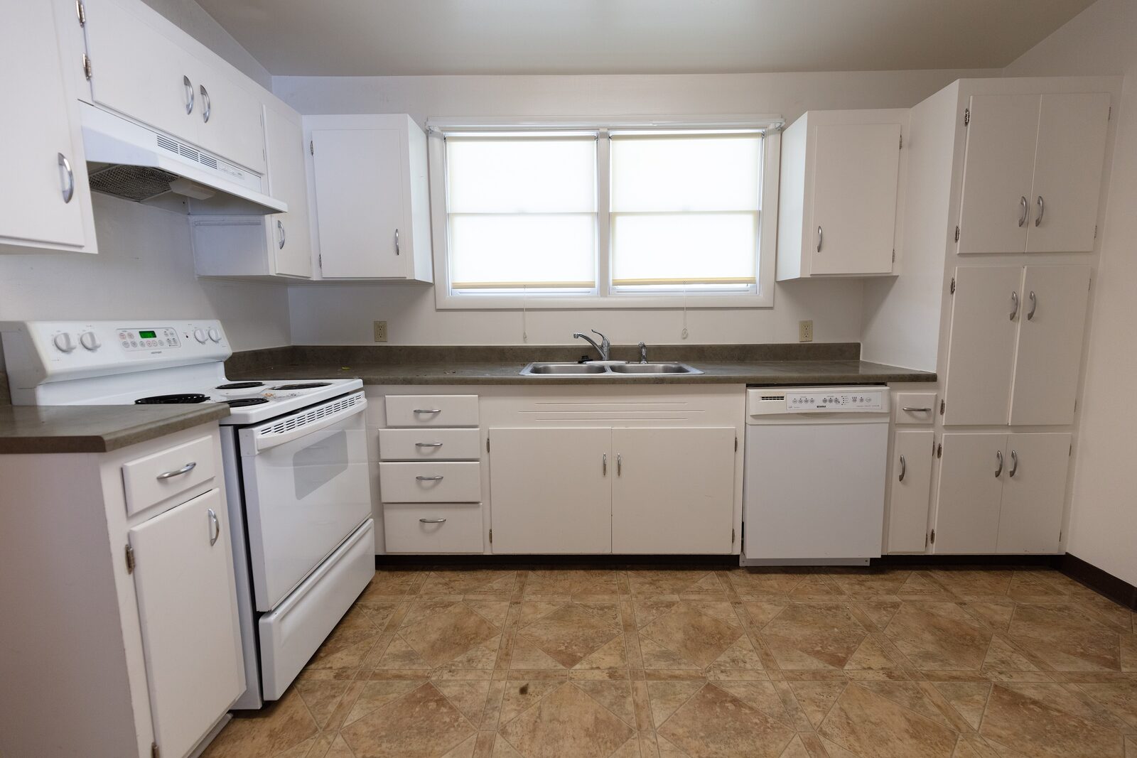 The original kitchen with white laminate cabinets and worn vinyl flooring