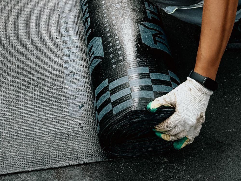 Roofer unrolling a new membrane across a flat roof
