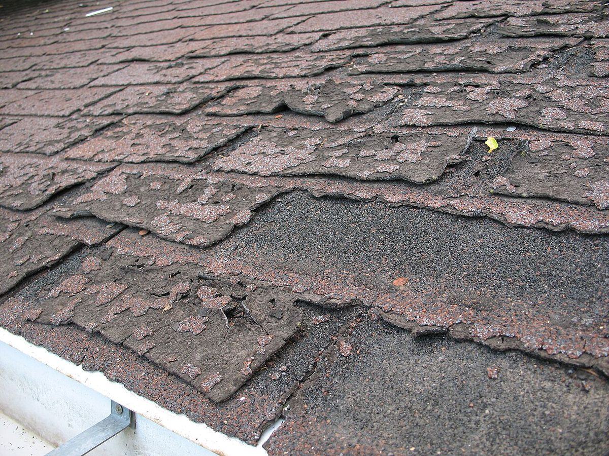 Old brown asphalt shingles, curled and cracked along the edges
