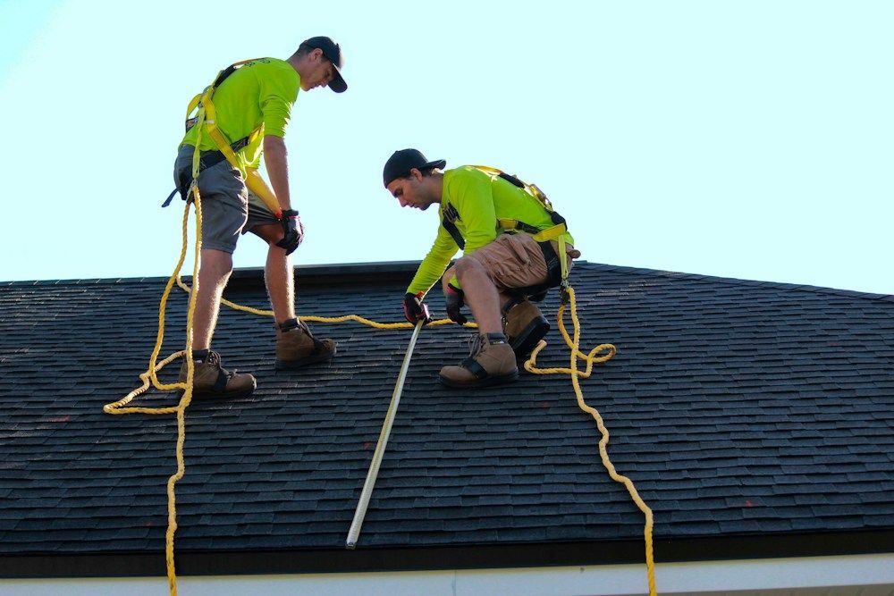 Two roofers in safety harnesses working on a new charcoal shingle roof