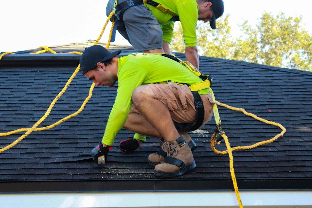 Roofers in harnesses fastening new shingles after a hailstorm