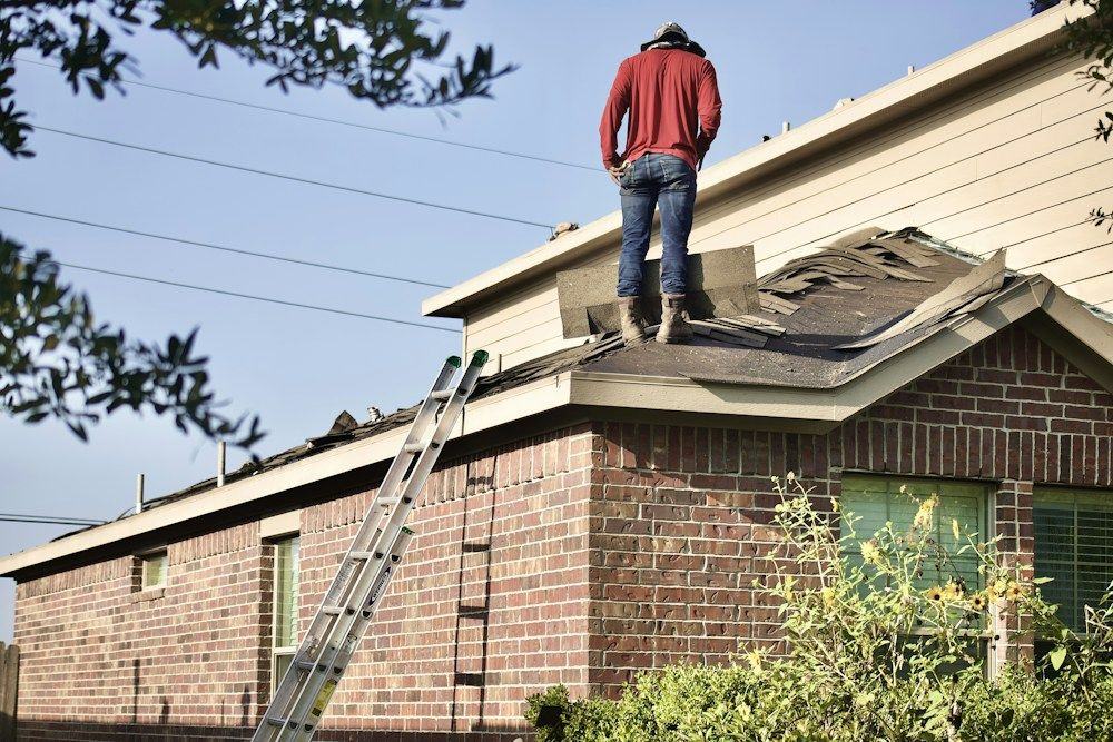 Roofer standing on a partially torn-off roof of a brick house