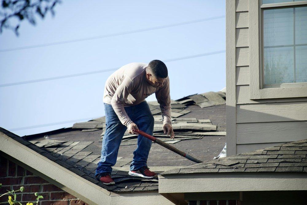 Roofer tearing old shingles off a house roof with a shovel