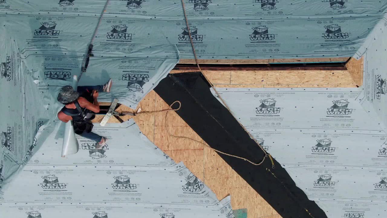 Peak Roofing crew member installing synthetic underlayment on a steep roof