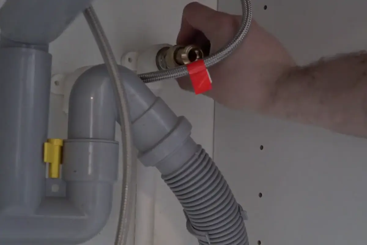 A plumber's hand connecting a braided steel supply line to a shutoff valve under a sink