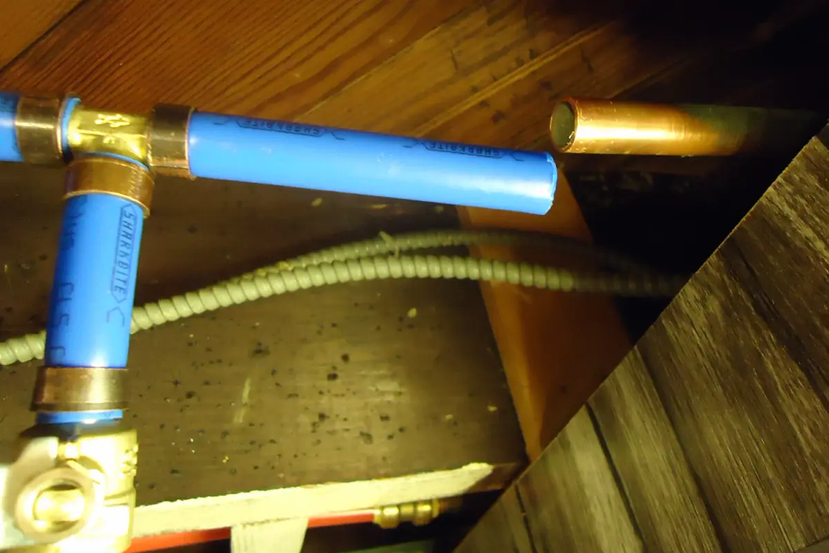 Blue PEX water lines with brass fittings and a shutoff valve running between floor joists