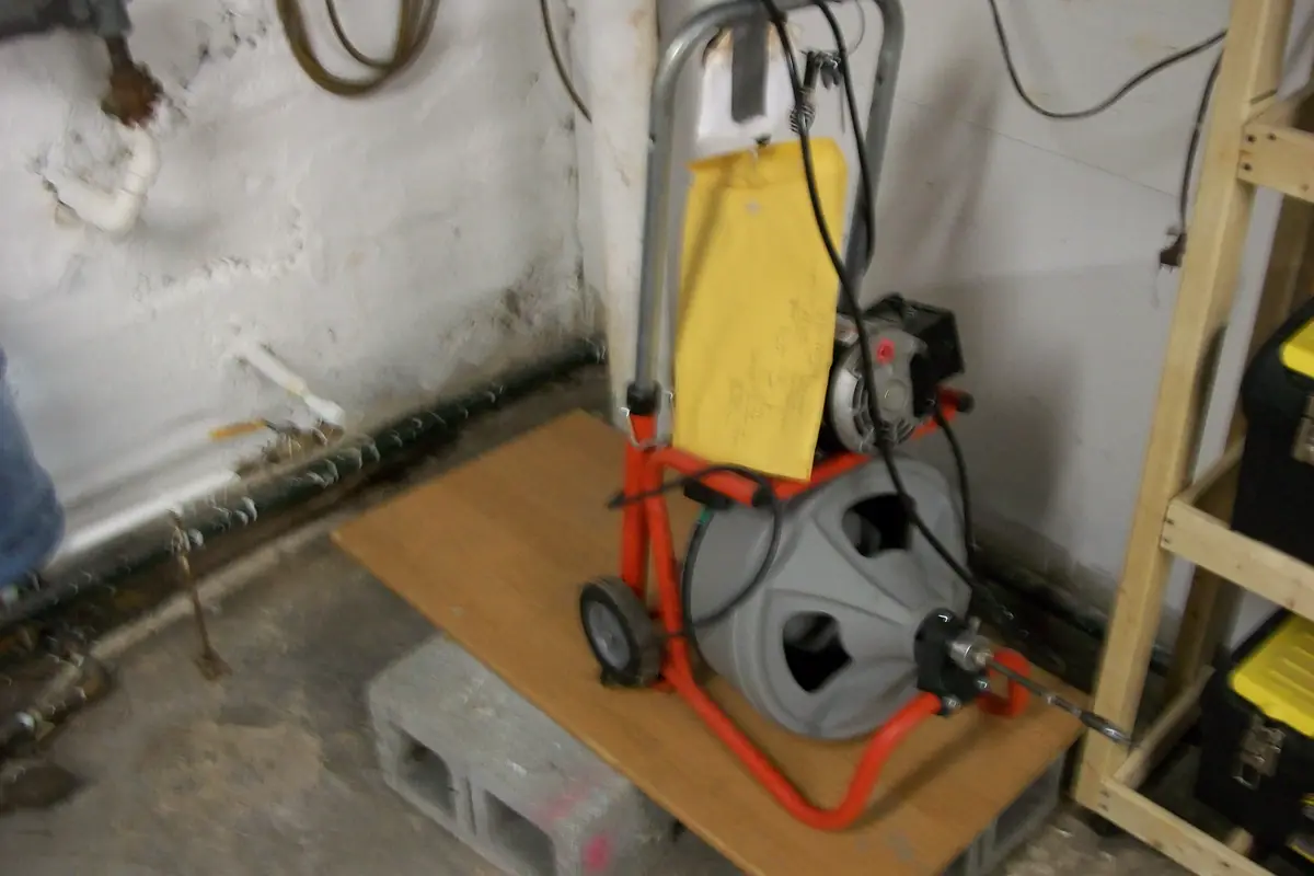 A sectional drain cleaning machine on a wooden platform in a basement utility area