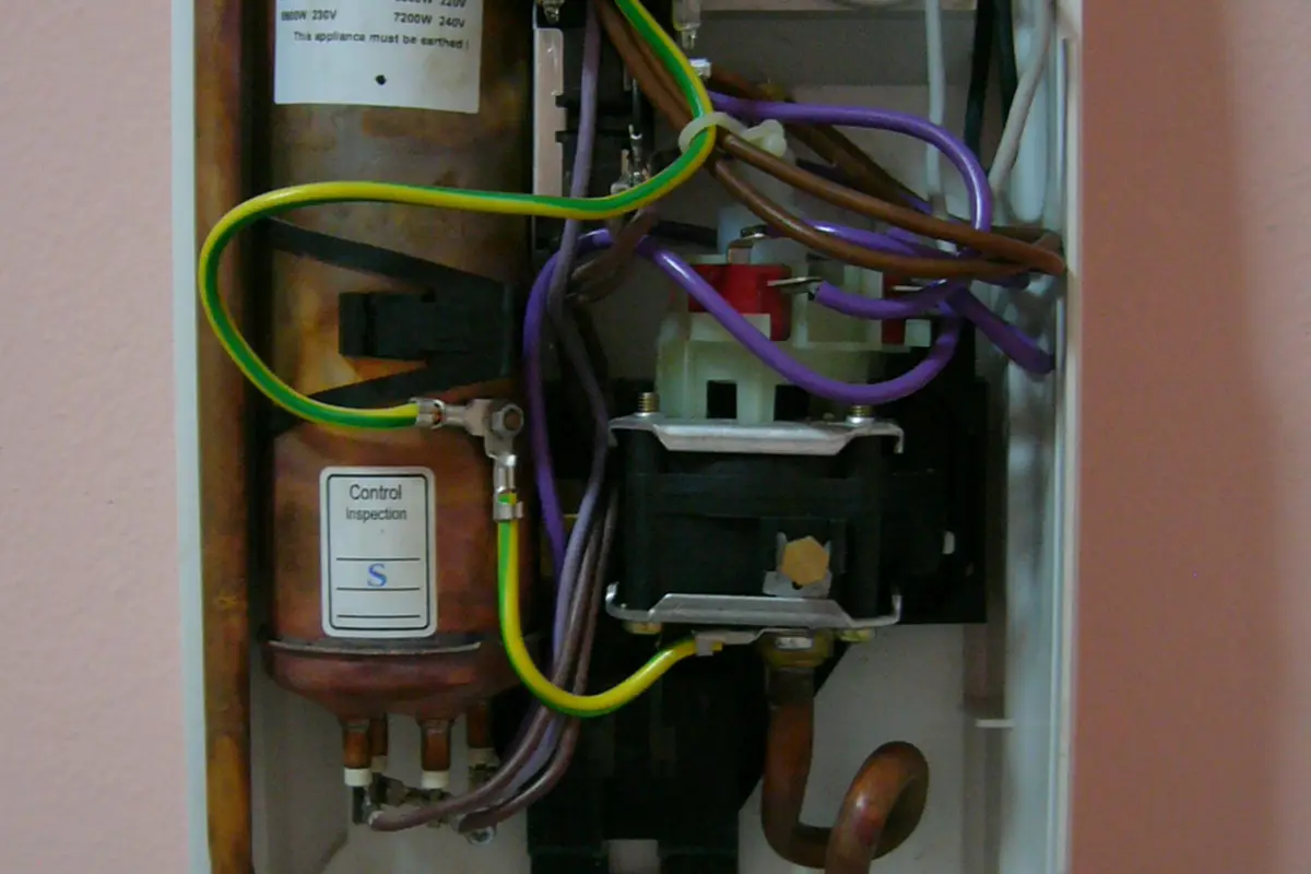 The inside of an electric tankless water heater with its cover off, showing copper heating chambers and wiring