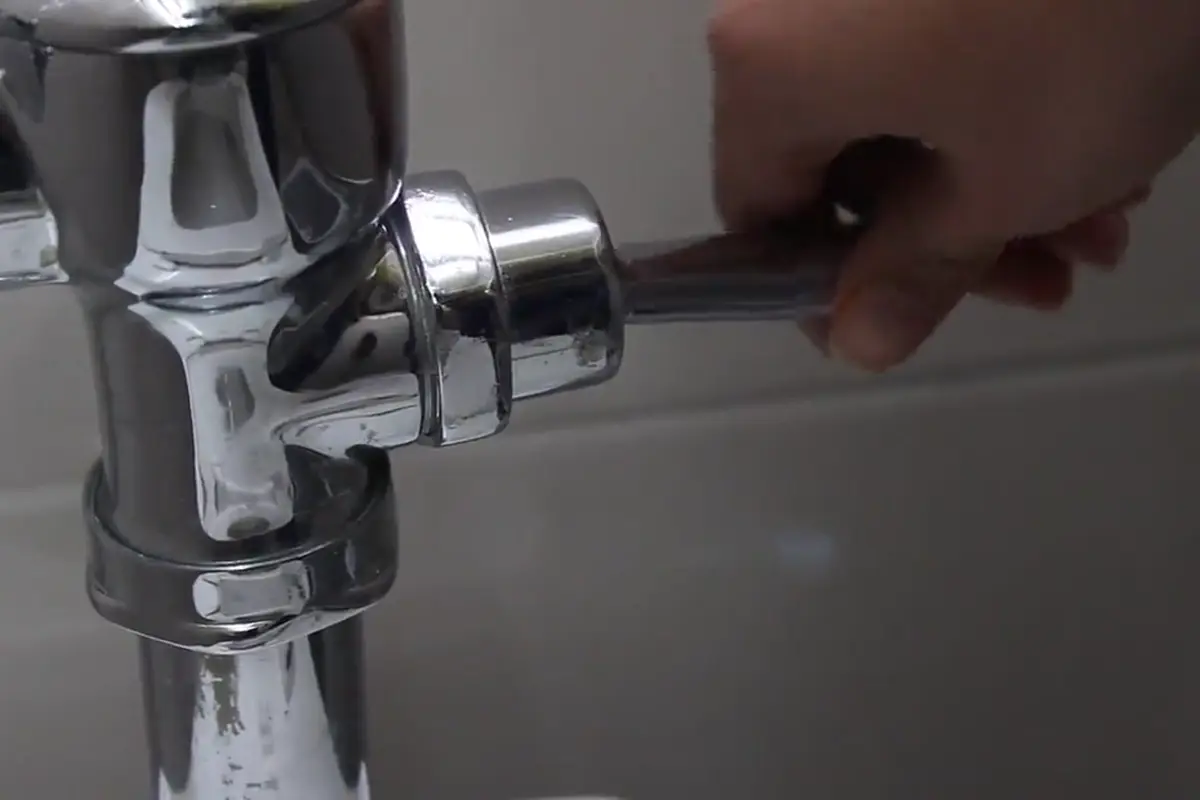 A plumber tightening a chrome toilet flush valve with an adjustable wrench