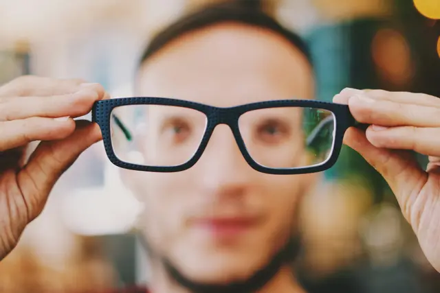 Man holding up a pair of black rectangular eyeglasses
