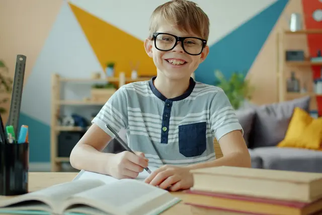 Boy wearing glasses smiling while doing homework